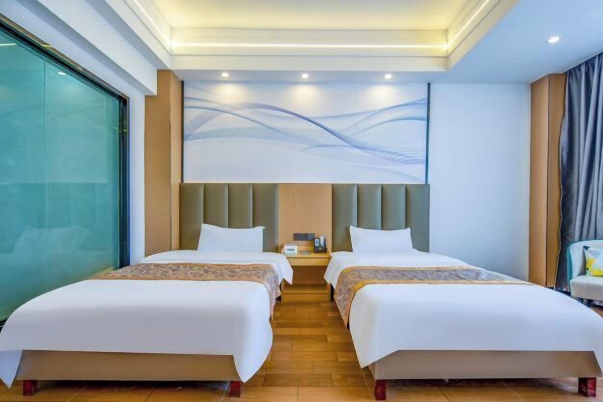 A hotel room with two beds, a large window, a modern wall art piece, and a nightstand with a lamp.
