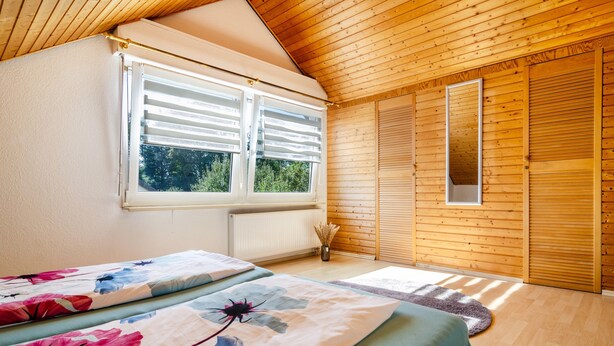 A bedroom with a wooden ceiling, a window with shutters, a radiator, and a bed with floral bedding. - Apartment 'Fewo Georg' with Wi-Fi (Pfullendorf)