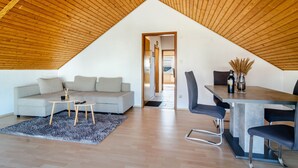 A modern loft with a sloped ceiling, a sofa, a dining table with chairs, and a kitchen area. - Apartment 'Fewo Georg' with Wi-Fi (Pfullendorf)
