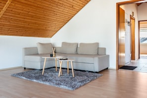 A modern living room with a sloped ceiling, a grey sofa, a small round table, and a grey rug.