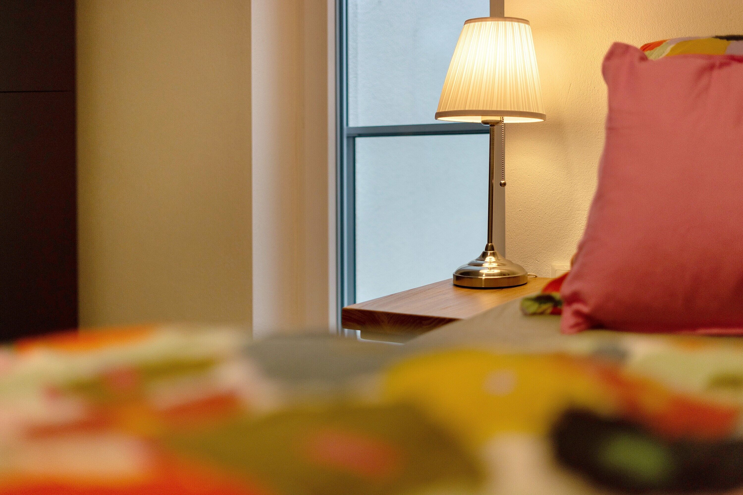 Ein Nachttisch mit Lampe, Kissen und einem Bett mit bunter Decke.