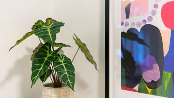 Ein Blumentopf mit breiten Blättern, ein gerahmtes abstraktes Gemälde und eine weiße Wand.