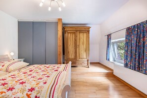 A bedroom with a bed, a wardrobe, a window with curtains, and a radiator.