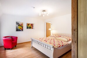 A bedroom with a bed, a red chair, and two paintings on the wall.