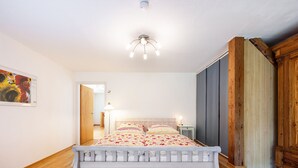 Ein Schlafzimmer mit einem weißen Bett, Holzboden, einer Deckenleuchte und einem Holzschrank.