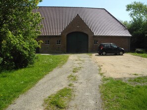 A brick building with a tiled roof, a large door, and a car parked in front.