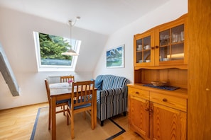 A room with a dining table, chairs, a sofa, a cabinet with glass doors, and a window with a view of greenery.