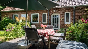 Ein Backsteinhaus mit Ziegeldach, einer Terrasse mit Tisch und Stühlen sowie einem grünen Sonnenschirm.