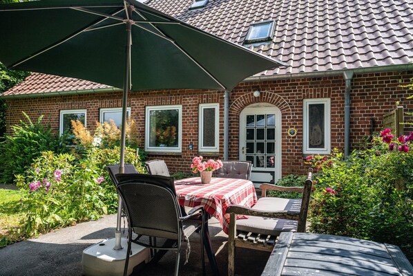 A brick house with a tiled roof, a patio with a table and chairs, and a green umbrella.