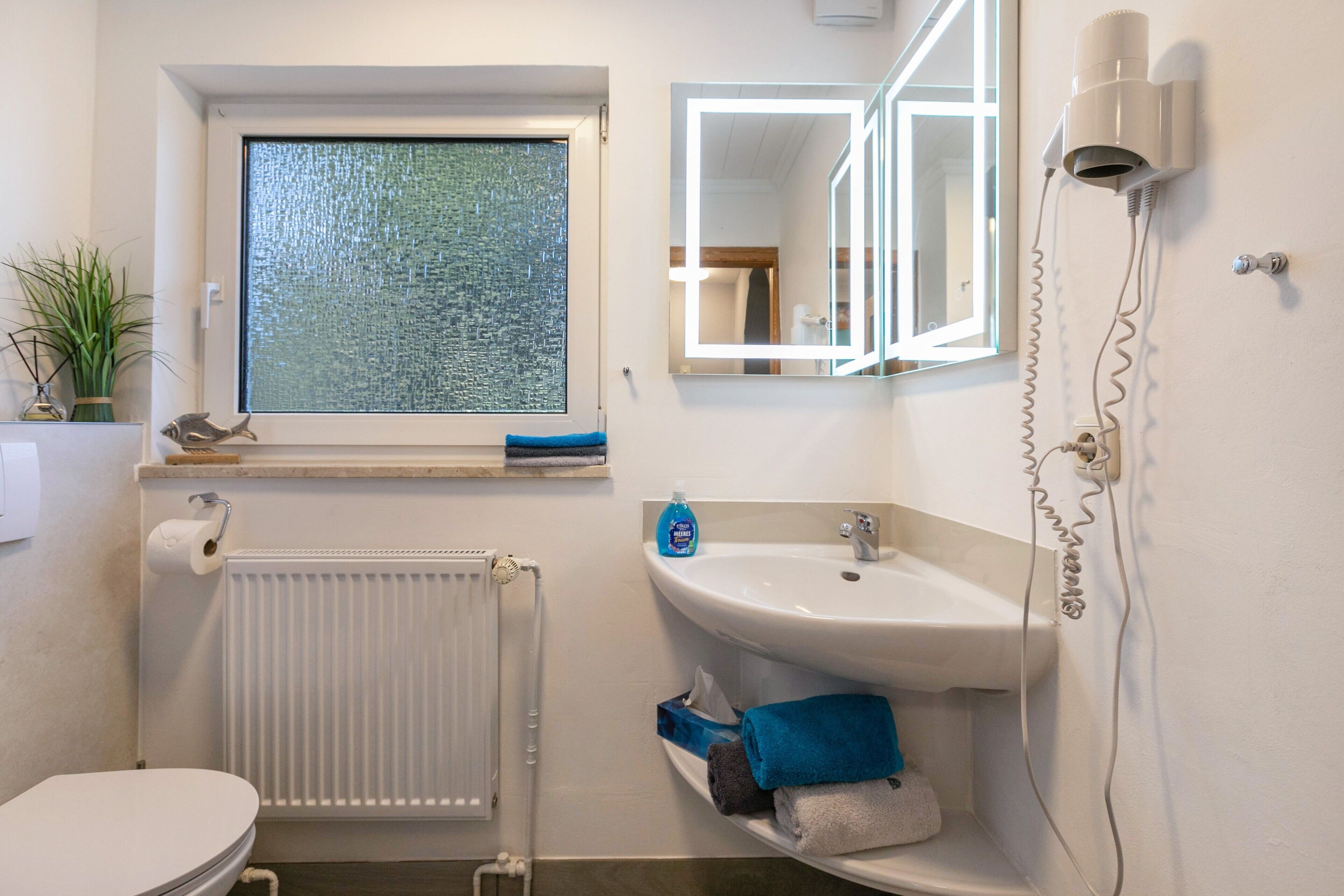 Un baño con inodoro, radiador, lavamanos, espejo y ventana con vistas.