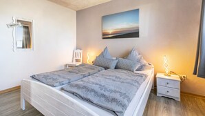 Ein Doppelbett mit floralem Überwurf, ein Nachttisch mit Lampe, ein Wandbild und ein Spiegel mit einem Schild.