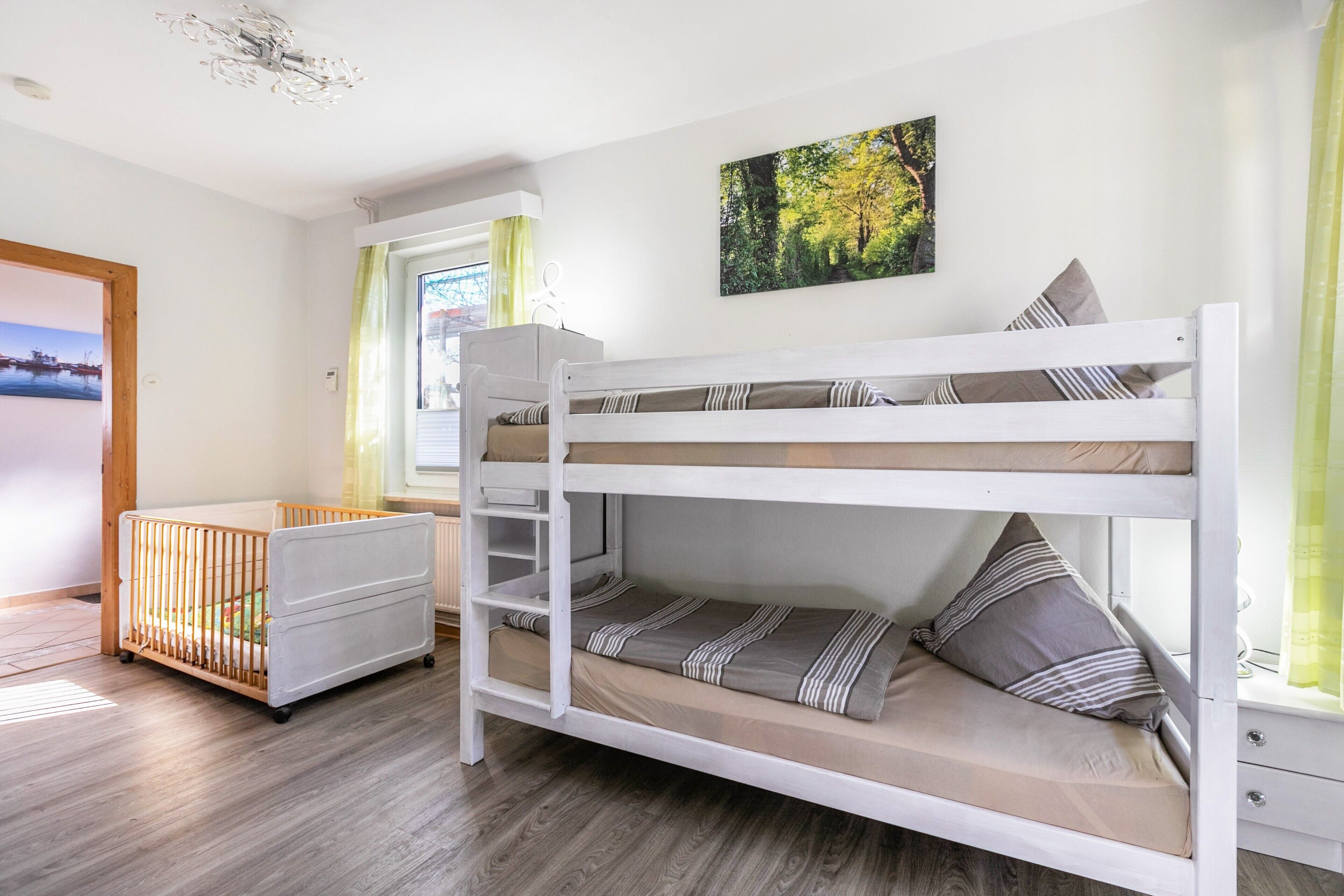 Una cama individual superpuesta con una cuna incorporada, una ventana con cortinas y un cuadro en la pared.