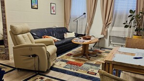 Un salon comprenant un canapé, un fauteuil, une table basse et une table à manger sur laquelle se trouvent des papiers.