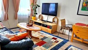Un salon avec un canapé, une table basse en bois, un téléviseur, une plante et une bibliothèque.