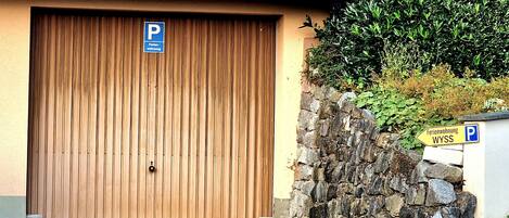 A closed wooden garage door with a blue parking sign above it, a stone wall, and a sign indicating 'Ferienwohnung WYSS' to the right.