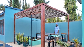 Un espace extérieur abrité, doté d’une pergola en bois, de plantes en pot, ainsi que d’une table et de chaises.