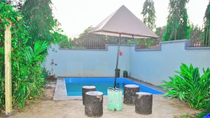 Une piscine dont le bord est bleu, entourée d’un petit muret et d’un espace abrité comprenant une table et des chaises.