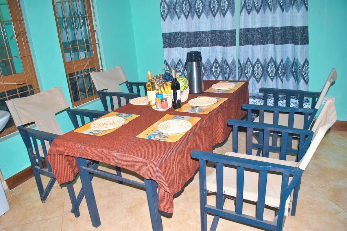 A dining area with a table set for six, chairs, a coffee maker, and various food items.