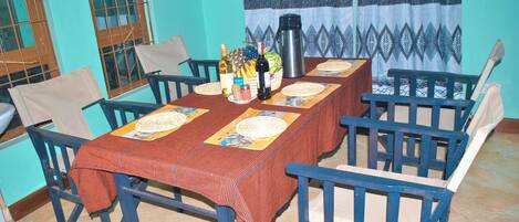 A dining area with a table set for six, chairs, a coffee maker, and various food items.