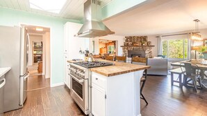 A modern kitchen with a central island, a dining area with a stone fireplace, and a view of the outdoors.