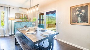 A dining area with a wooden table, chairs, and a bench. There is a window with a view of greenery outside.