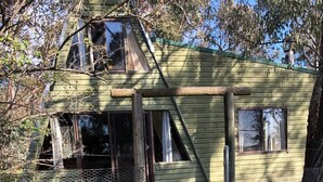 Una casa de dos pisos con fachada verde, un muelle de madera y una cerca de malla metálica.