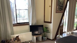Una sala de estar con televisor, sofá, ventana con cortinas, planta y un cuadro en la pared.