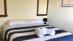 Una cama bien hecha con ropa de cama azul y blanca, una toalla enrollada y un cuadro en la pared.