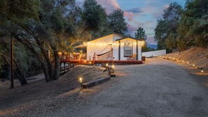 Uma cabana moderna de um andar, com varanda e iluminação externa, rodeada por árvores.