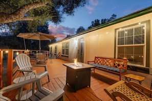 An outdoor deck with wooden furniture, a fire pit, and string lights. - Big Backyard with games, hot tub, Firepit, Deck, Views (Oakhurst)
