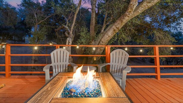 Um deck externo com lareira, duas cadeiras Adirondack e luzes de corda.