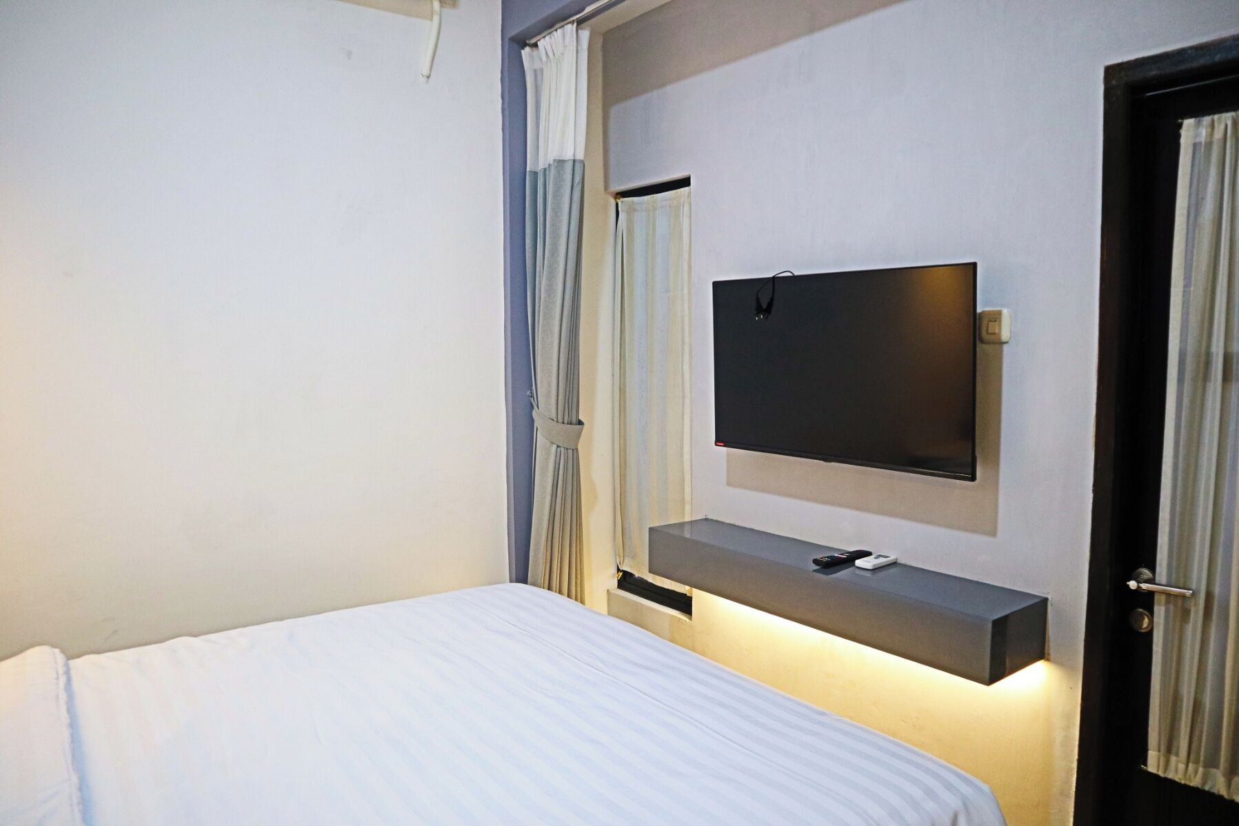 A hotel room with a bed, a mounted TV, and a door.
