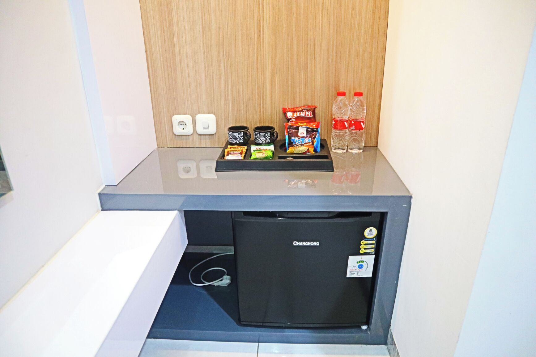 Un mini refrigerador con aperitivos, una botella de agua y un enchufe.