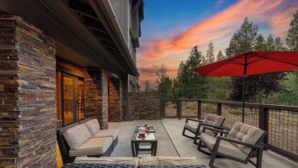 A patio with wicker furniture, a red umbrella, and a stone wall. - Prime Location Near Skiing | Luxe All-Season Retreat by AvantStay (Truckee)