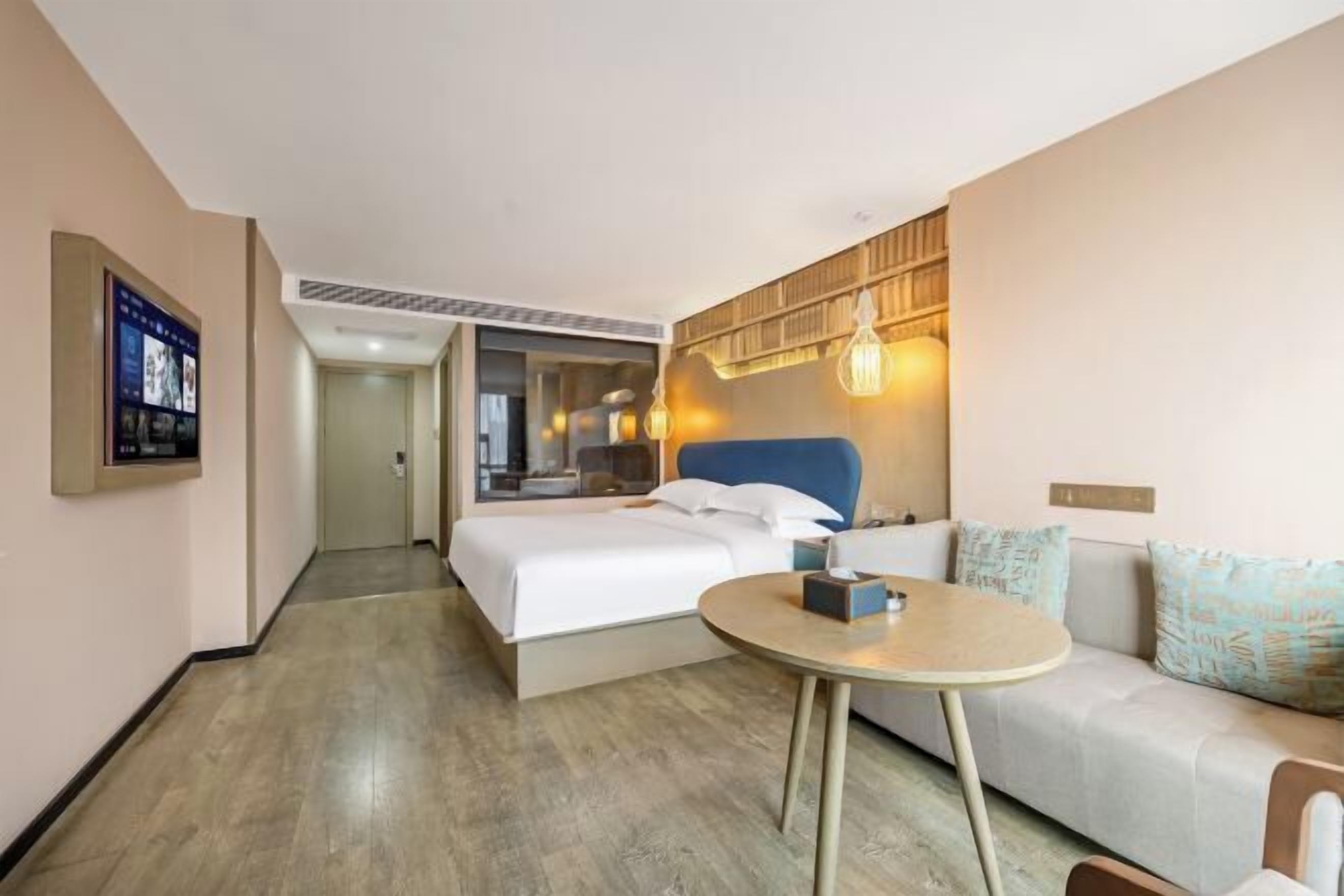 Une chambre d’hôtel avec un lit, une table ronde, un canapé et un téléviseur fixé au mur.