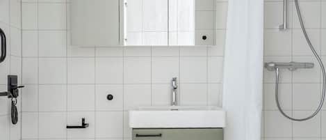 A bathroom with a toilet, sink, mirror, shower, and a cabinet.
