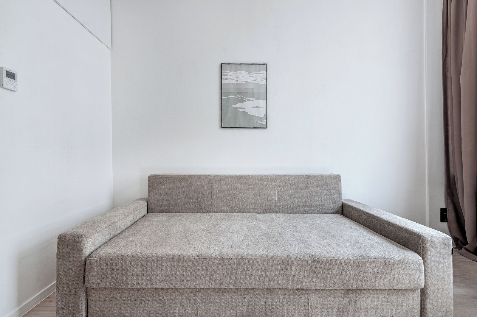 Un divano grigio in una stanza con un muro bianco e un quadro incorniciato sopra.