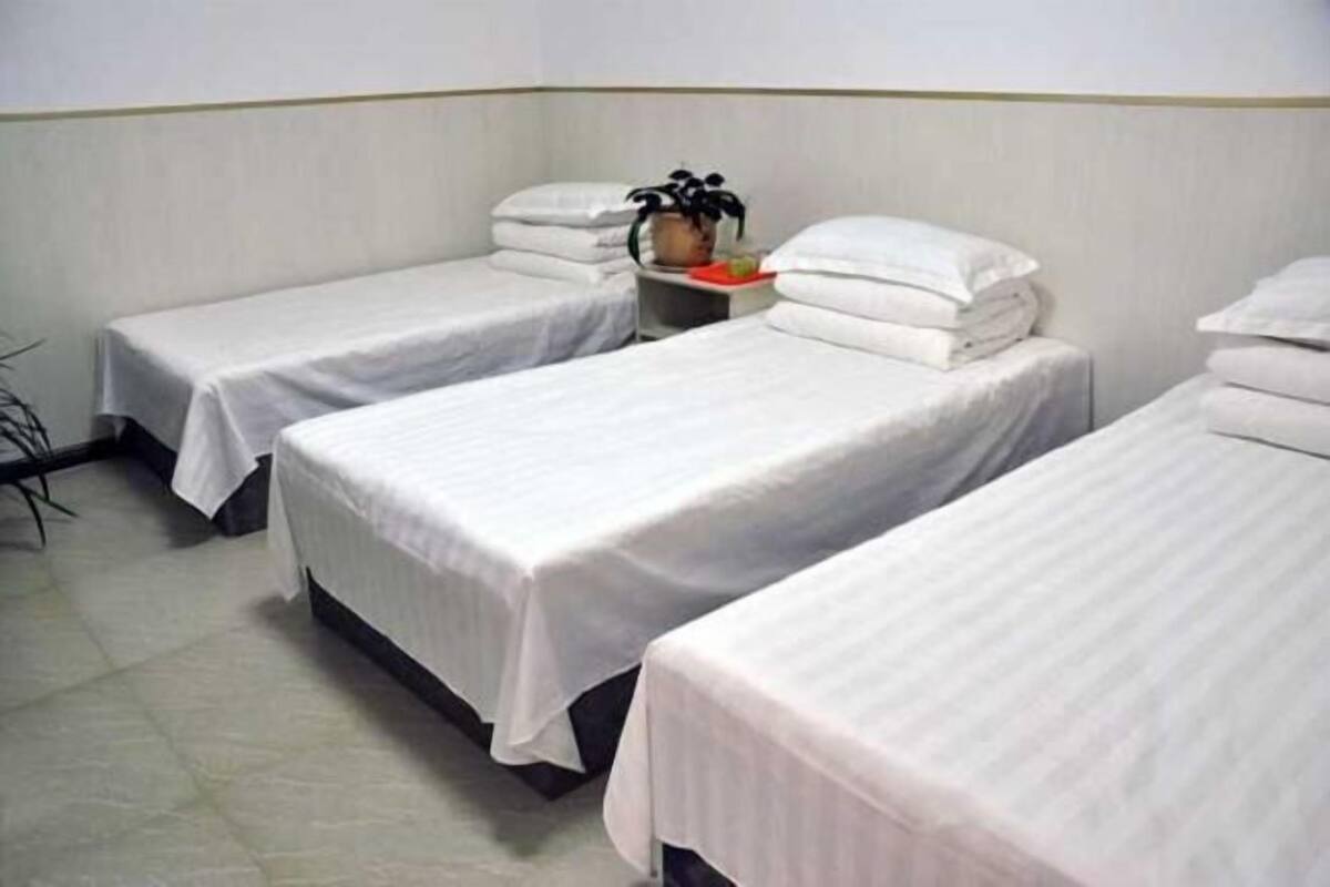 Een hotelkamer met drie eenpersoonsbedden, elk voorzien van witte beddengoed en kussens. Er staat een klein tafeltje met een plant en een dienblad met spullen.