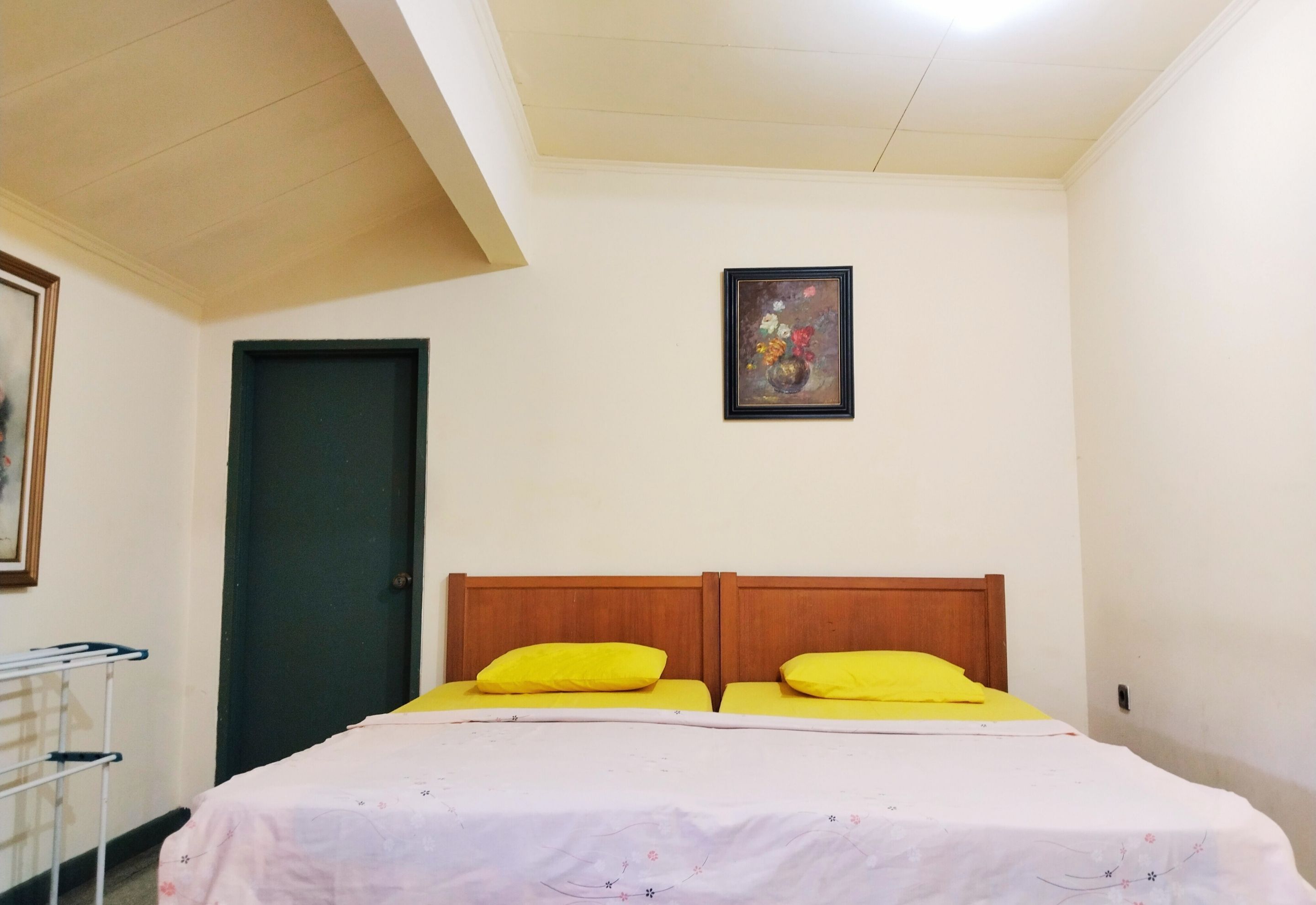 A room with a bed, a door, a framed picture on the wall, and a ceiling light.
