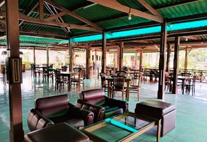 Een ruime binnenruimte met meerdere tafels en stoelen, een glazen salontafel, en een groen dakconstructie.
