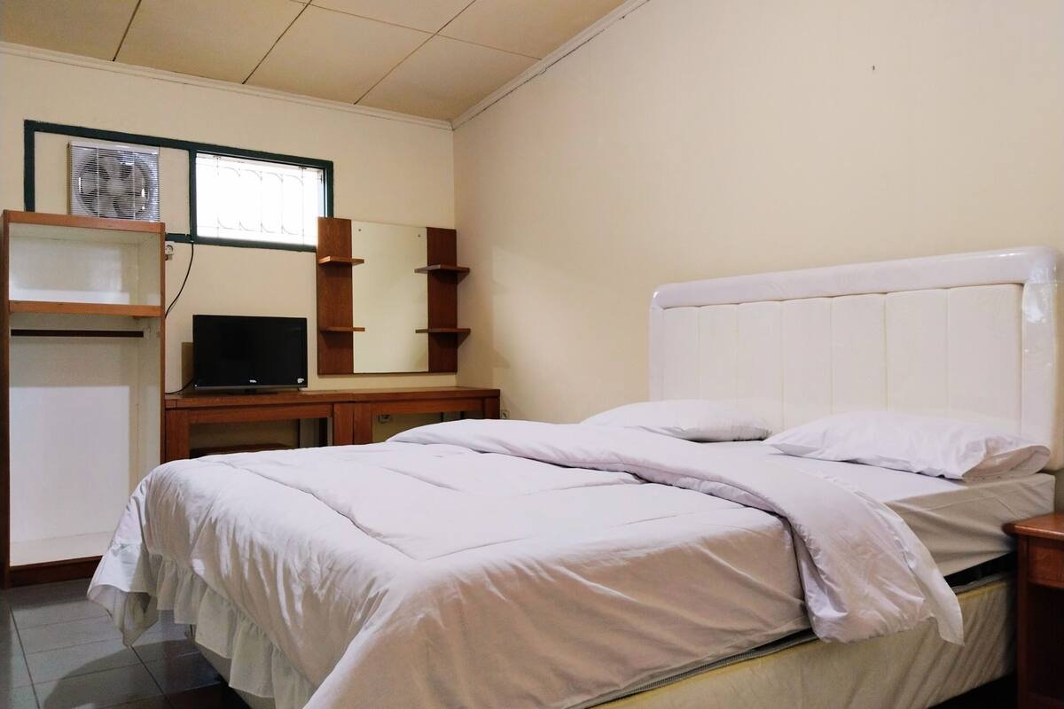 Een slaapkamer met een bed, een televisie, een bureau en een raam.
