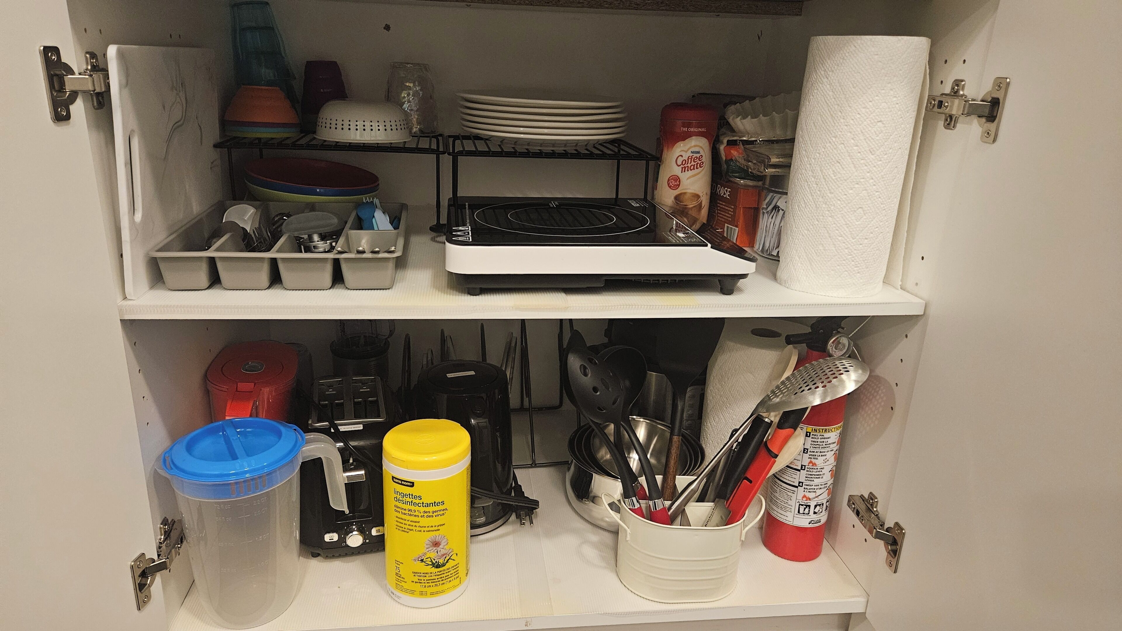 A kitchen cabinet with utensils, a coffee maker, and cleaning supplies.