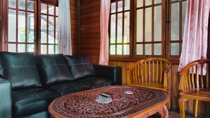 A room with a black leather sofa, a wooden table with intricate carvings, and wooden chairs. - Hotel New Sabrina (Cisarua)