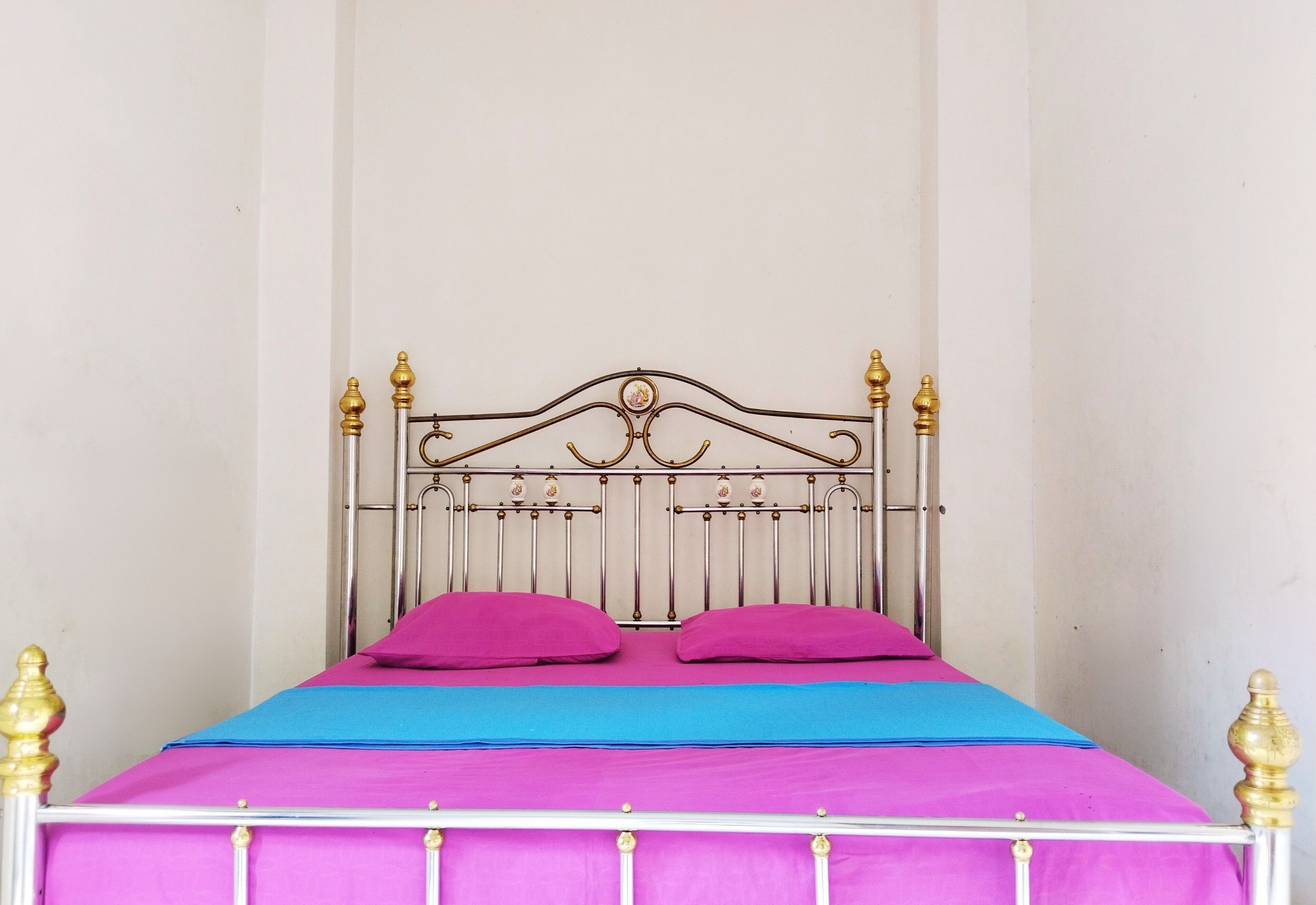 A bed with a metal frame and a headboard, two pillows, and a blue and pink bedspread.