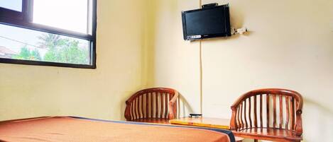 A room with a bed, two wooden chairs, a small table, a television mounted on the wall, and a window.