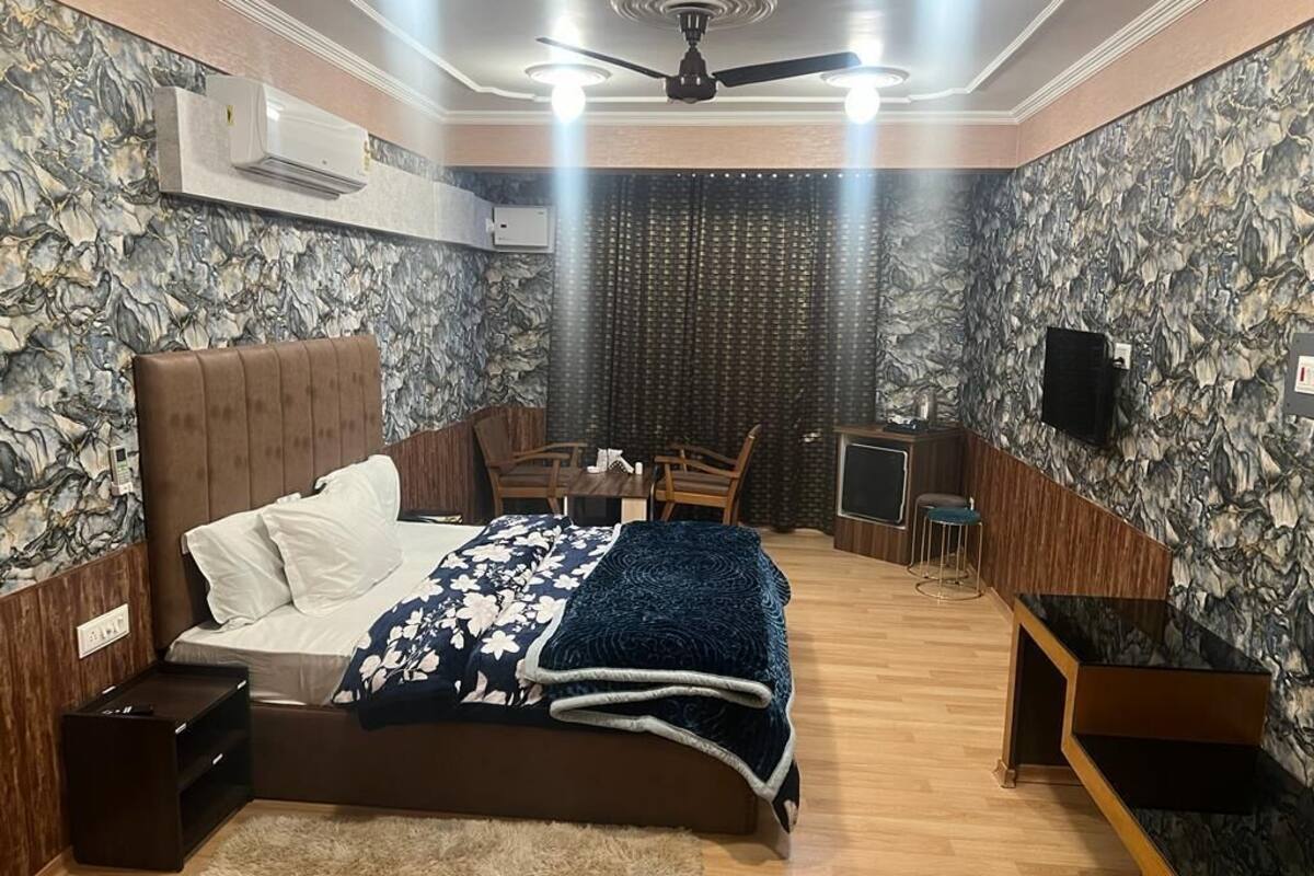 A bedroom with a bed, a desk, a chair, a TV, and a ceiling fan.