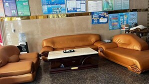 A seating area with two brown leather sofas and a matching armchair, a marble coffee table, and a wall with various informational posters.