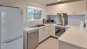 Een moderne keuken met witte kasten, een inbouw vaatwasser, een roestvrijstalen koelkast, een magnetron en een kookplaat.