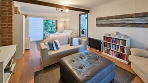 Een moderne woonkamer met een bank, voetenbankje, boekenkast en een bed met uitzicht op het groen.