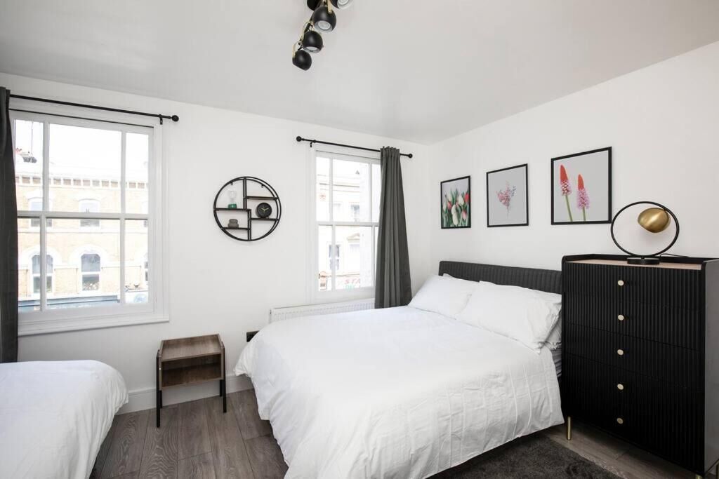 A bedroom with a large bed, a small bedside table, a dresser, and a window with curtains.
